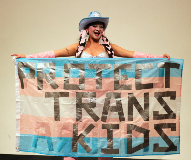 Student stands with trans flag that reads Protect Trans Kids
