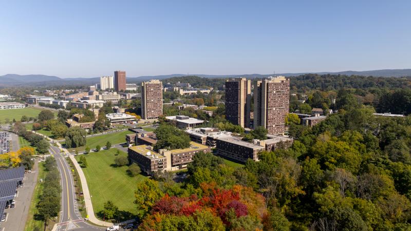 Aerial view of Umass Amherst campus in fall. Tall brown brick buildings, green grass, red and green leaves