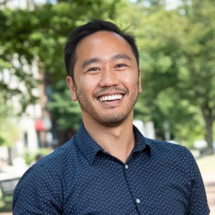 Daniel Do smiles at the camera wearing a blue shirt with a white dot pattern.