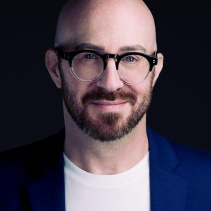 Ethan Haymovitz smiles at the camera wearing a white t-shirt, blue blazer and glasses.
