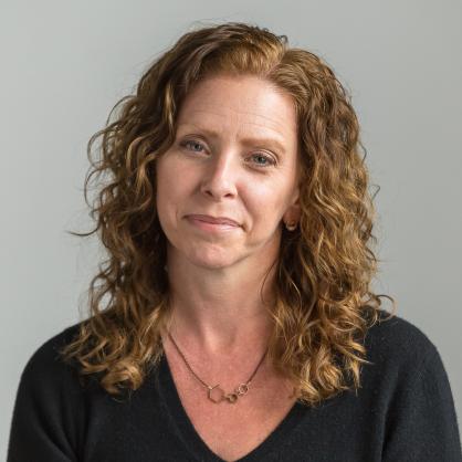 Sara Brackenbury looks at the camera wearing a black top with shoulder length wavy hair.