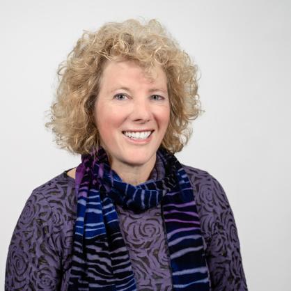 Marsha Kline Pruett smiles at the camera wearing a purple sweater and striped scarf.