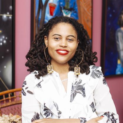 Loren Cahill stands in the Colored Girls Museum in Philadelphia wearing a black and white blouse. Her arms are folded in front of her.