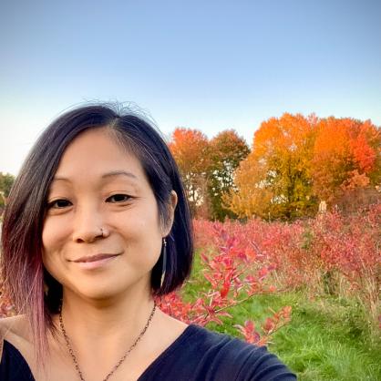 Sarai Engel stands in front of a field of fall foliage looking at the camera 