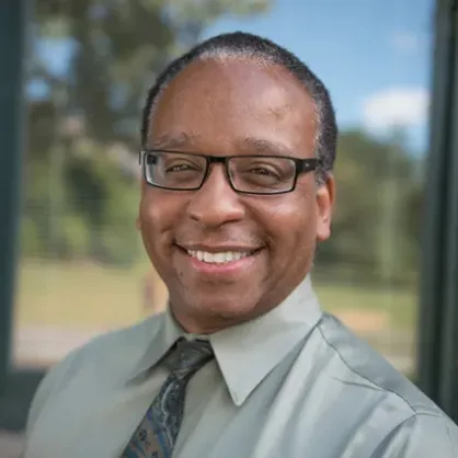 Nnamdi Pole smiling in grey collared shirt and glasses