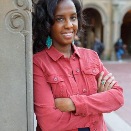Clarice Robinson wearing a coral shirt leaning against a carved cement wall with spirals