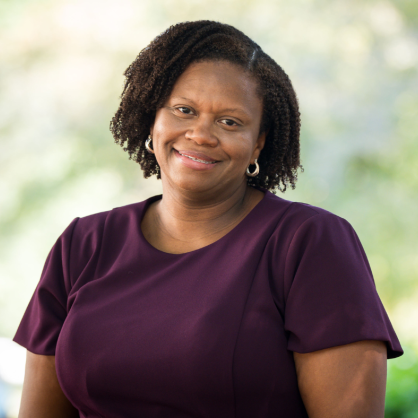 Cecily Davis wearing purple short sleeve shirt smiling with greenery behind