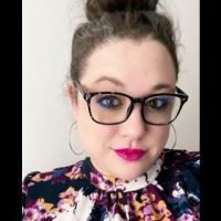 Amanda Sposato faces the camera wearing a floral top and glasses.