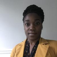 Alicia Peterkin looks at the camera wearing a yellow jacket and black top. 