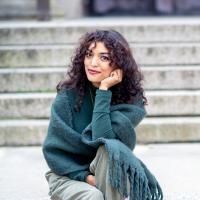 Photo of Ash Sabripour sitting on the steps to Seelye Hall with a green scarf wrapped around her.