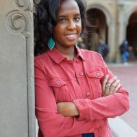 Clarice Robinson wearing a coral shirt leaning against a carved cement wall with spirals