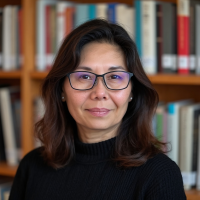 Maria del Pilar Bratko wearing glasses and black shirt smiles in front of bookcase