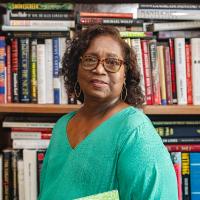 Rhoda Smith in front of a bookshelf wearing bright teal shirt