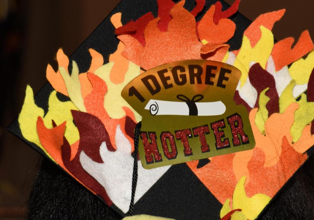 Photo of a mortar board reading 1 degree hotter and surrounded by paper flames. 