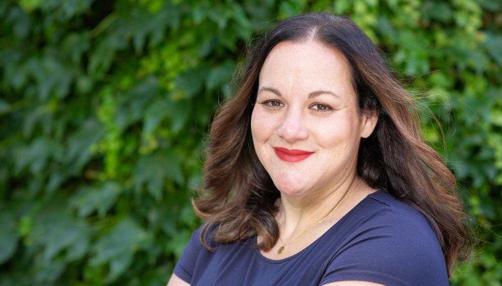 Professor Hannah Karpman smiles at the camera. She is wearing a blue top and her shoulder length brown hair is down. 