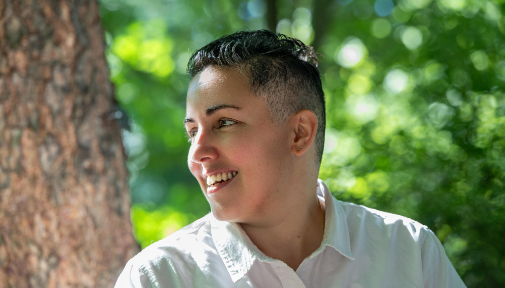 Lev Fein smiles looking off to the side. Behind is a tree and green leaves