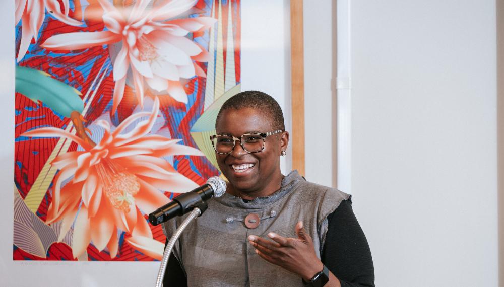 Lisa Moore speaking during her acceptance speech at the 2025 Alumni Awards. Behind a large painting of flowers