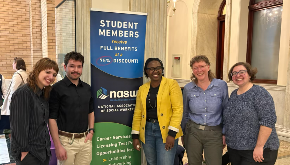 Five MSW students standing next to a poster that reads Student Members Receive Full Benefits at a Discount of 75% NASW National Association of Social Workers