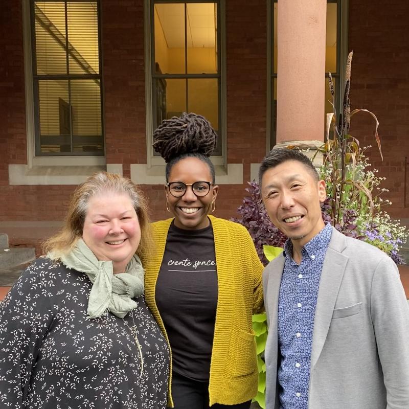 Katya Cerar, Arianne Napier-White, Kenta Asakura standing together in front of a brick