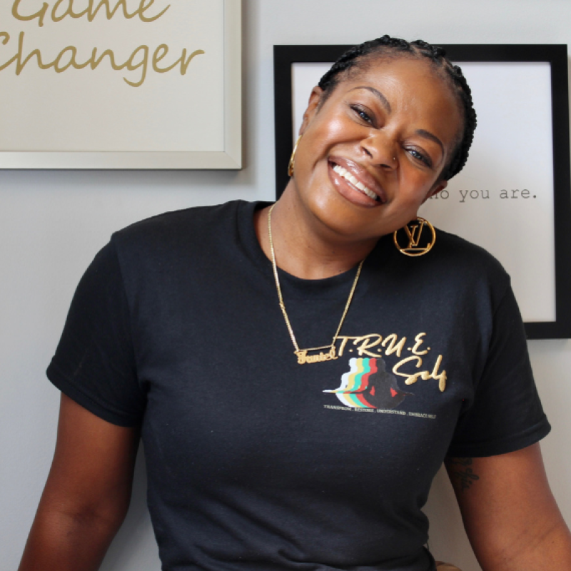 Nicole Faniel-Wilson wearing black tshirt smiling against grey wall with art hanging