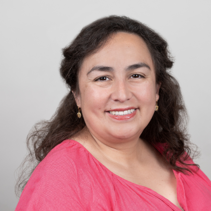 Maria Maldonado-Morales wearing bright pink shirt against grey wall smiling