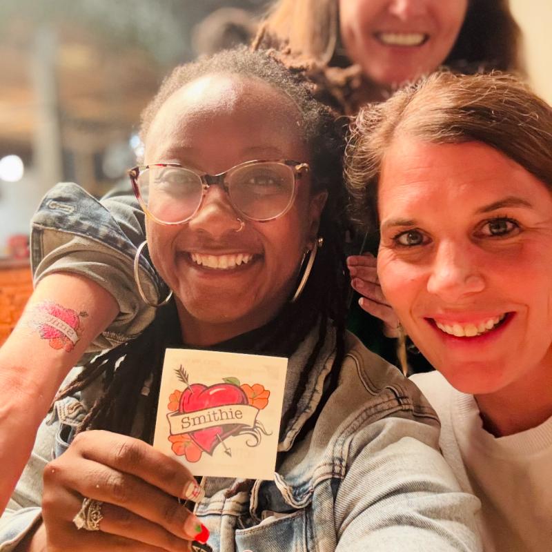 Janae Peters, Katie Potocnik Medina and Samantha Mishne hug, take selfie and Janae holds up a Smithie heart temporary tattoo
