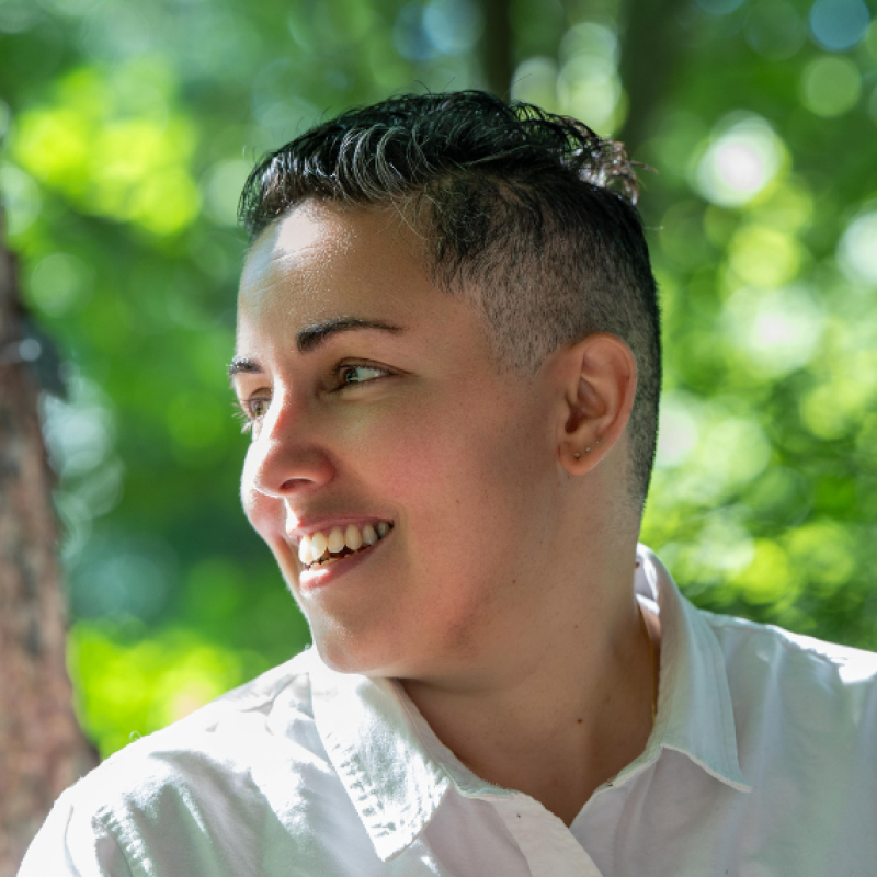 Lev Fein smiles looking off to the side. Behind is a tree and green leaves