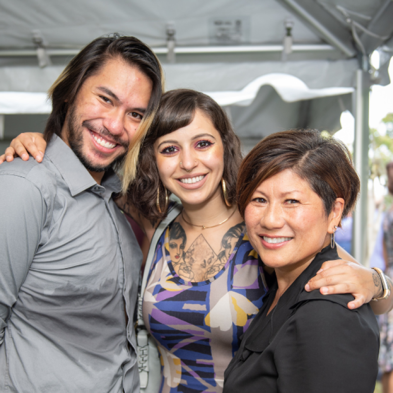 Marianne Yoshioka stands with two graduates with arms around each other