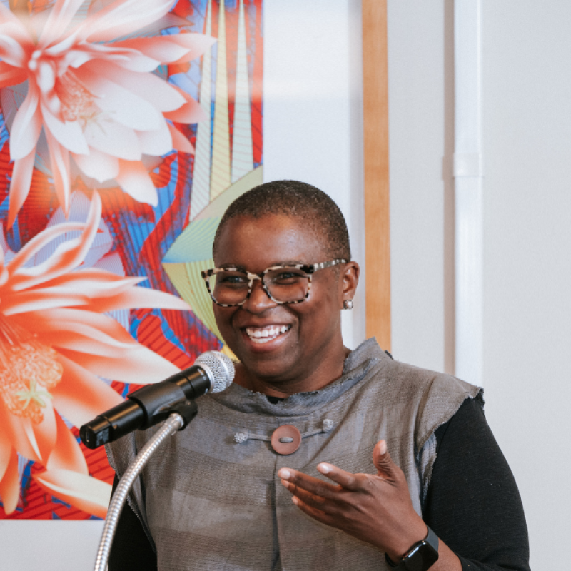 Lisa Moore speaking during her acceptance speech at the 2025 Alumni Awards. Behind a large painting of flowers