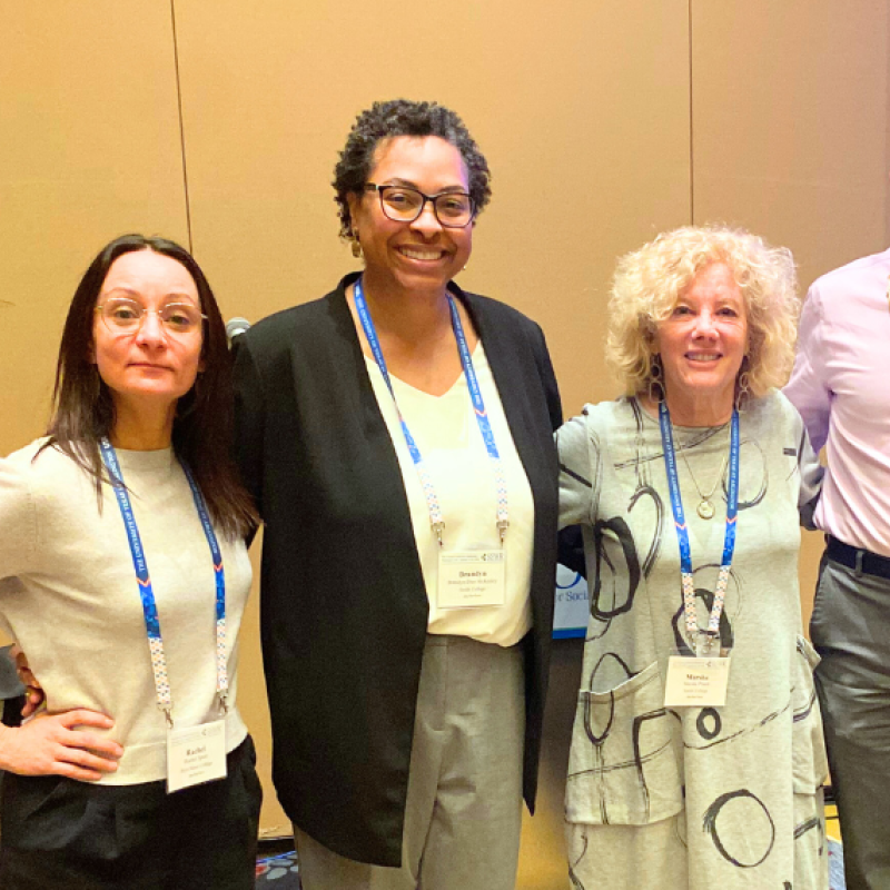 Five people including Brandyn-Dior McKinley and Marsha Pruett stand in a row with arms around each other with tan wall and large projector screen behind
