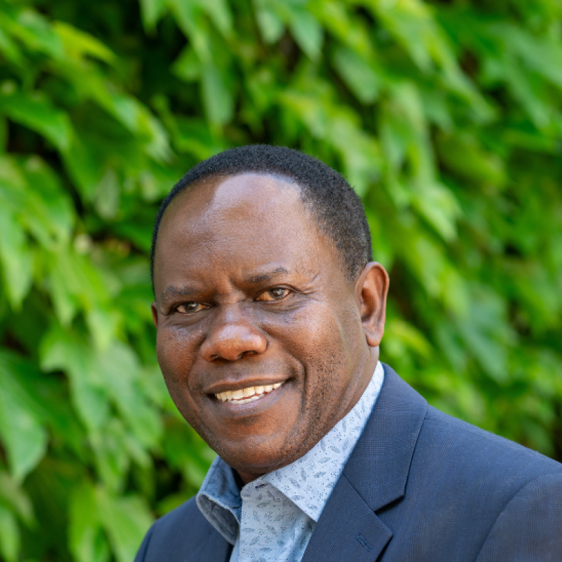 Hugo Kamya smiling against wall of ivy wearing dark blue suit