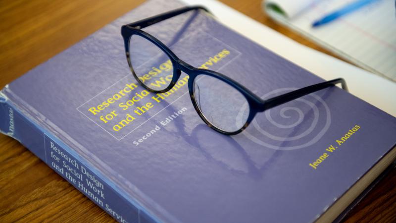 Image shows a pair of black frame glasses sitting atop a social work textbook.