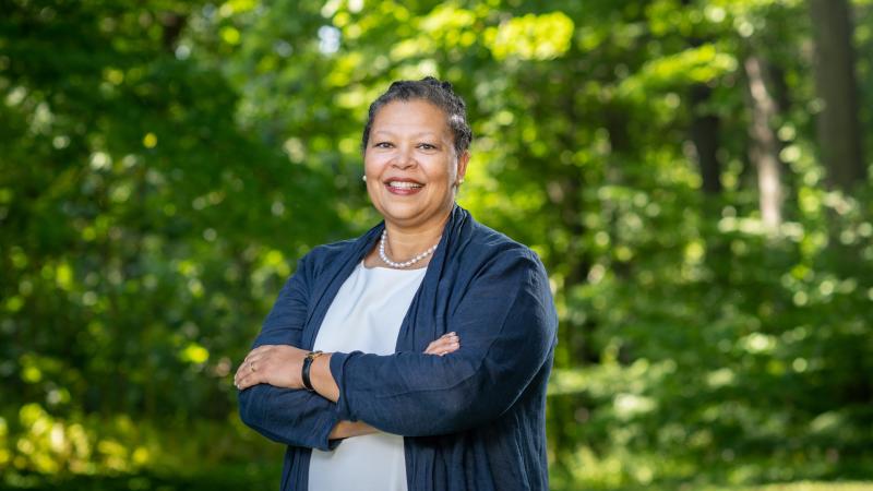 Portrait of incoming Smith College President Sarah Willie-LeBreton standing in front of green trees and wearing a blue top.