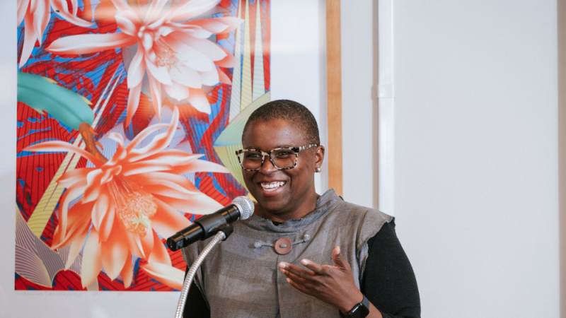 Lisa Moore speaking during her acceptance speech at the 2025 Alumni Awards. Behind a large painting of flowers