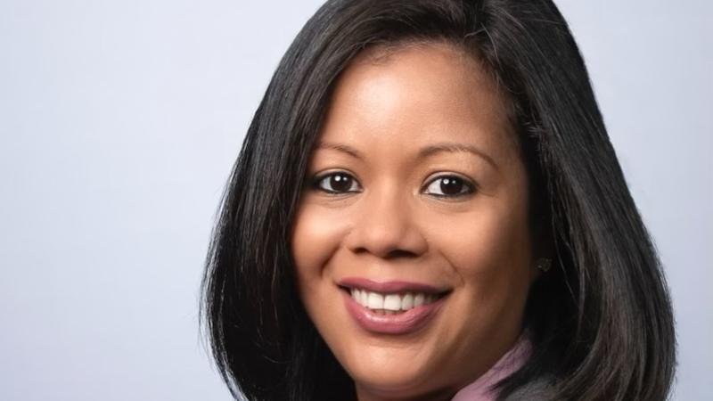 Cheryl Aguilar sits against white background wearing grey blazer and pink blouse with arms folded